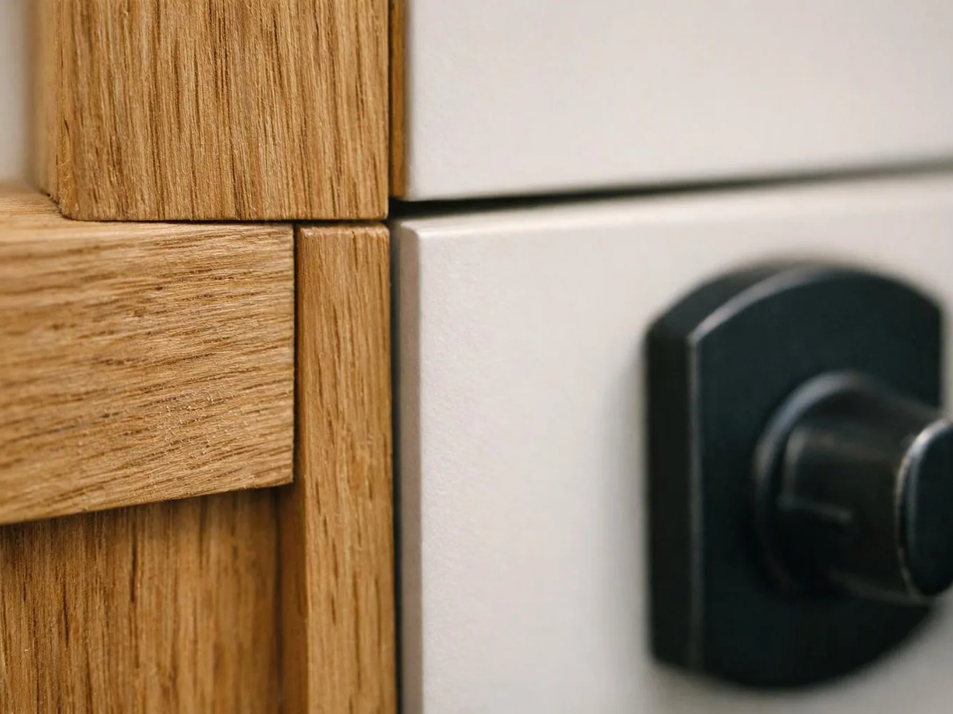 Close-up of a wooden cabinet corner beside a white panel and black knob