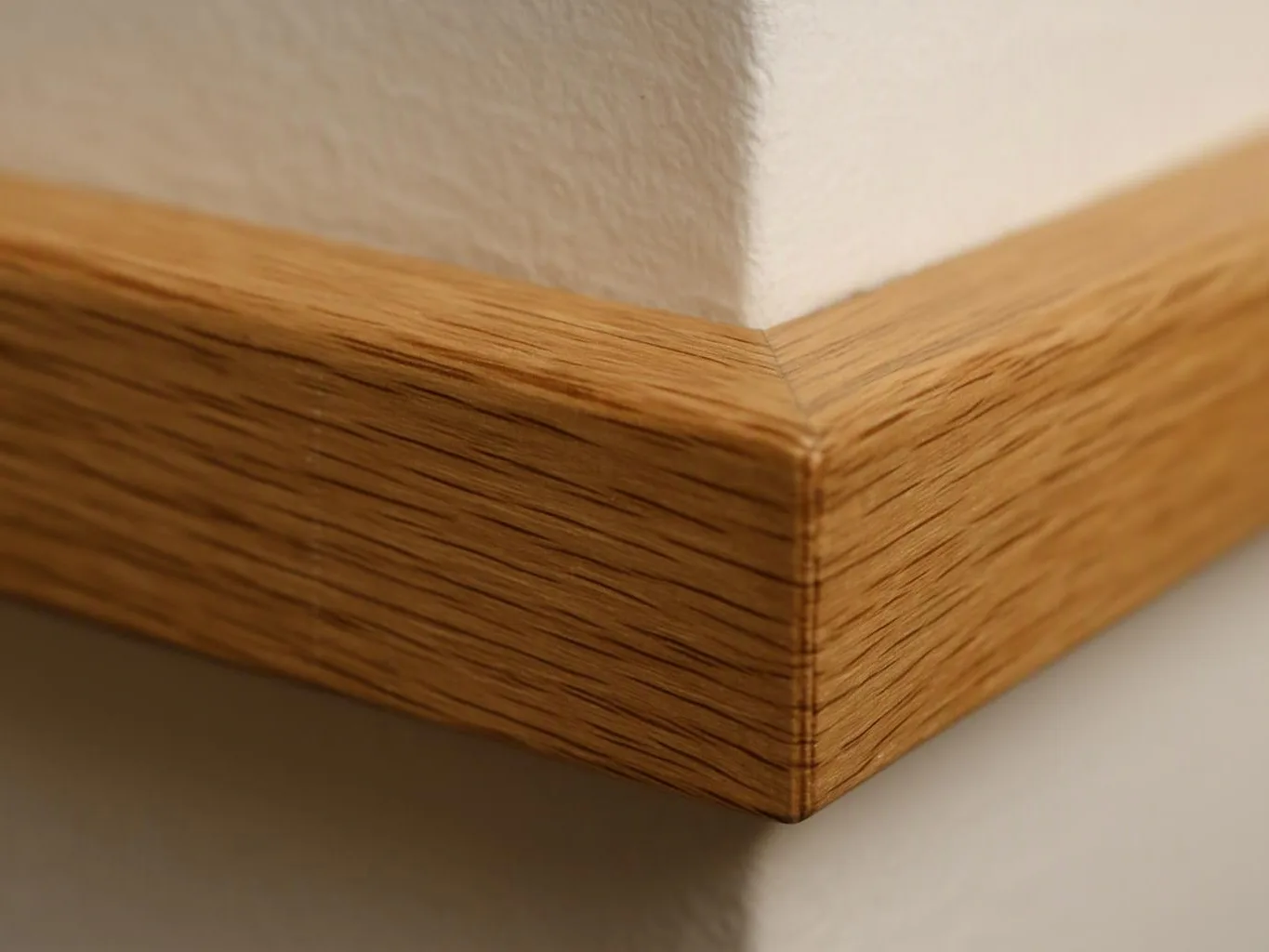 Close-up of a wooden wall trim corner against a white textured wall