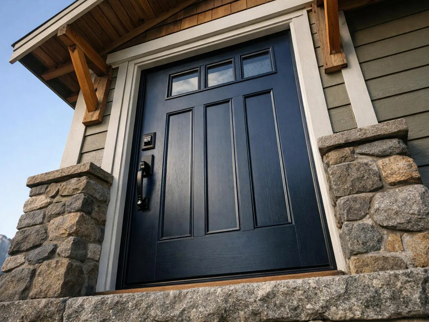 A dark blue front door with glass panes sits between stone pillars on a house exterior