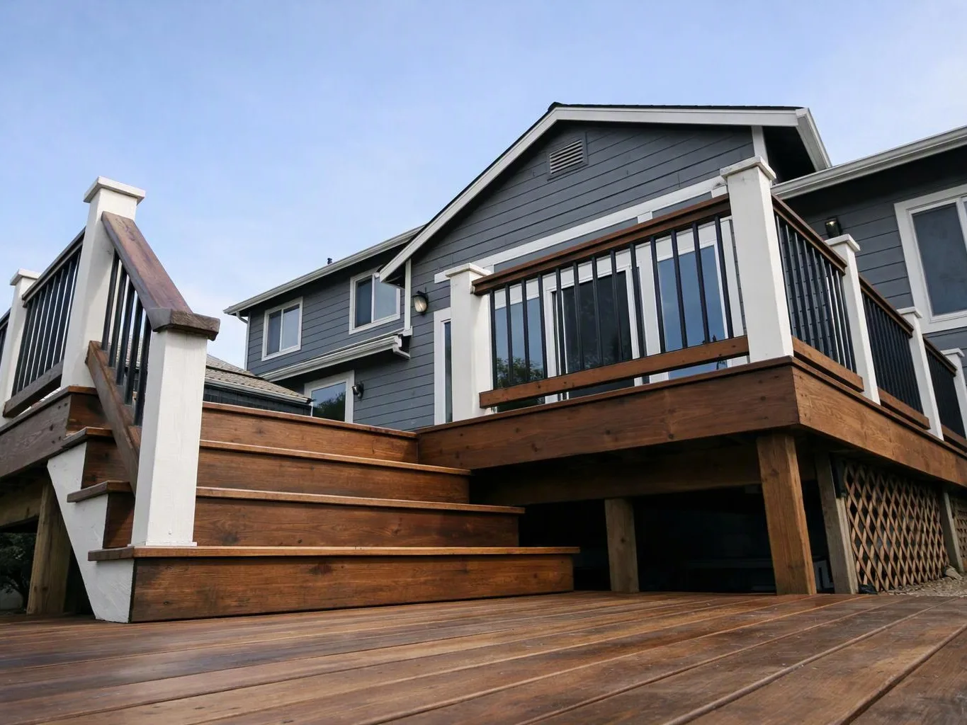 A gray house with a wooden deck and stairs rises against a clear blue sky