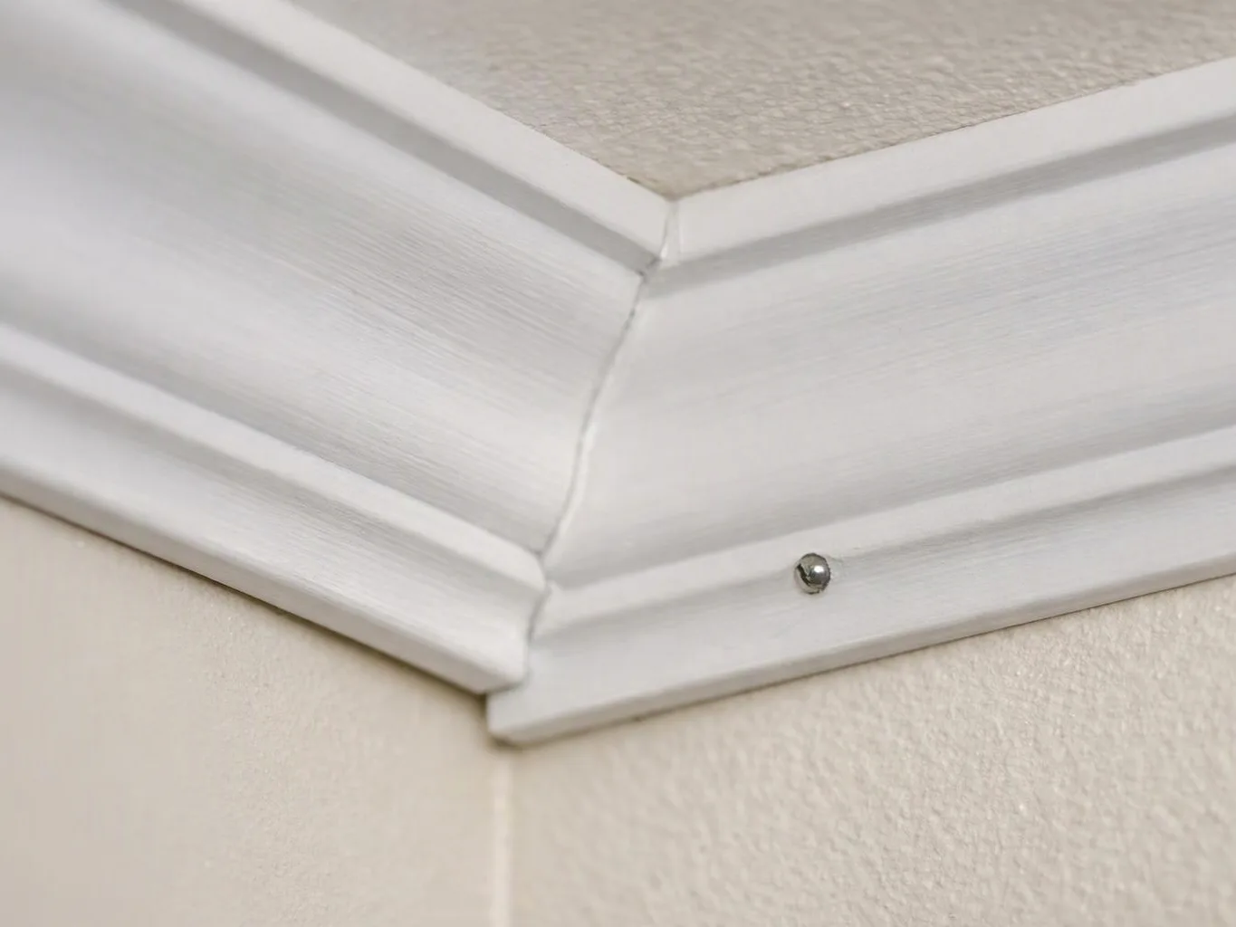 White crown molding meets at a wall corner, with a visible crack and one screw head